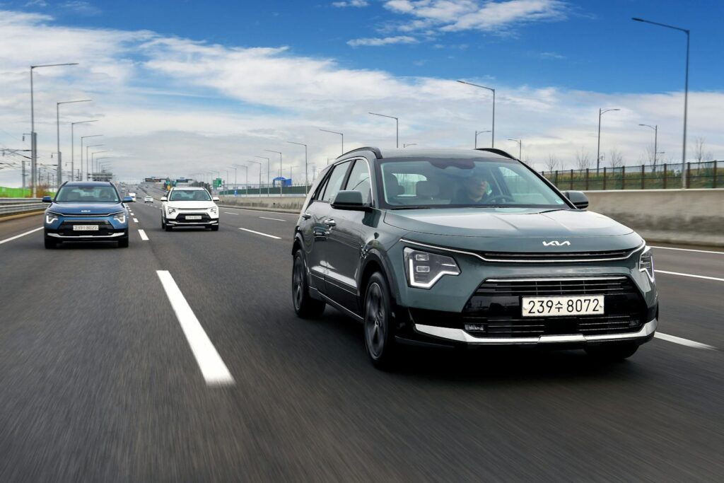 Kia Niro SUVs driving on a highway under a bright blue sky, showcasing speed and modern design.