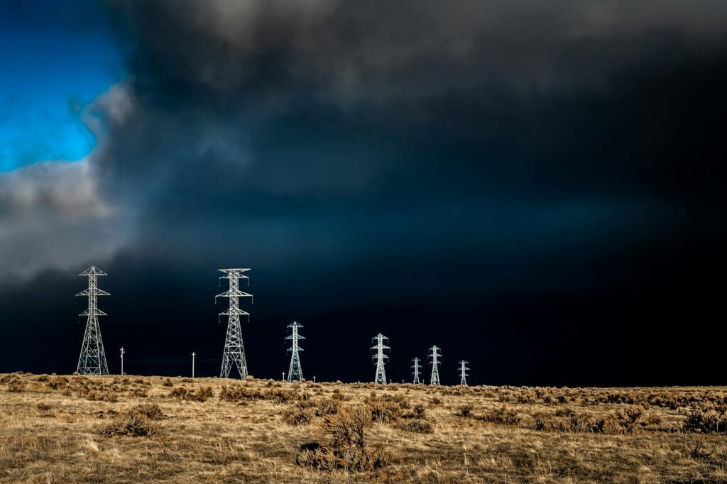 Power lines standing tall against dark storm clouds with a dramatic sky and open field.