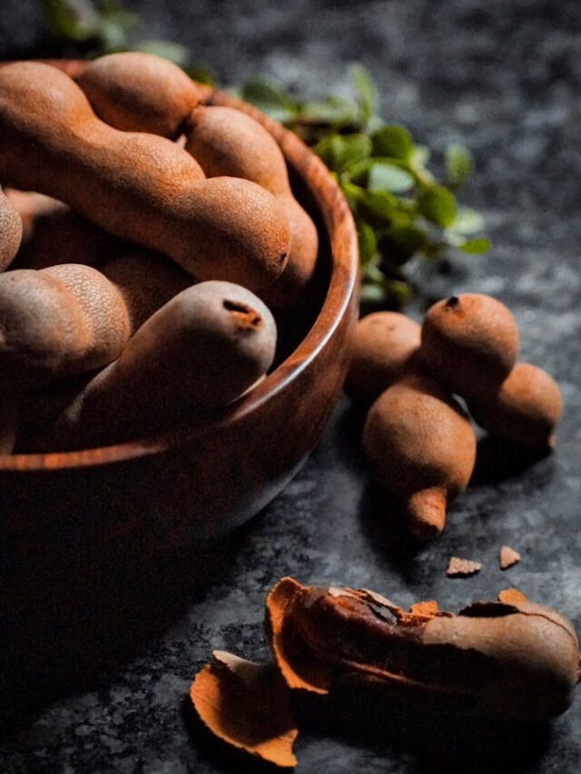 A rustic close-up of tamarind pods in a wooden bowl, showcasing their natural texture and earthy tones.